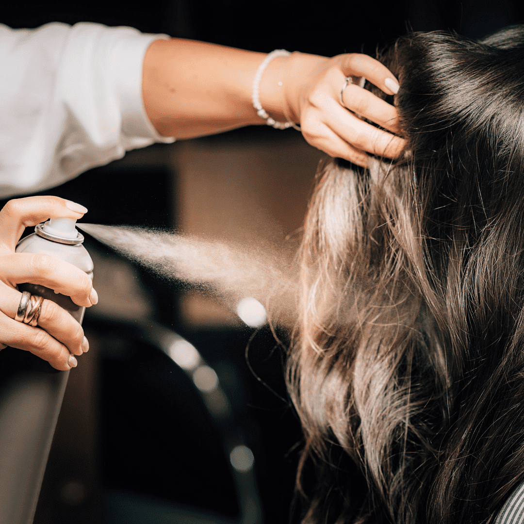 Hairdresser applying hairspray to a client's hair in a salon.