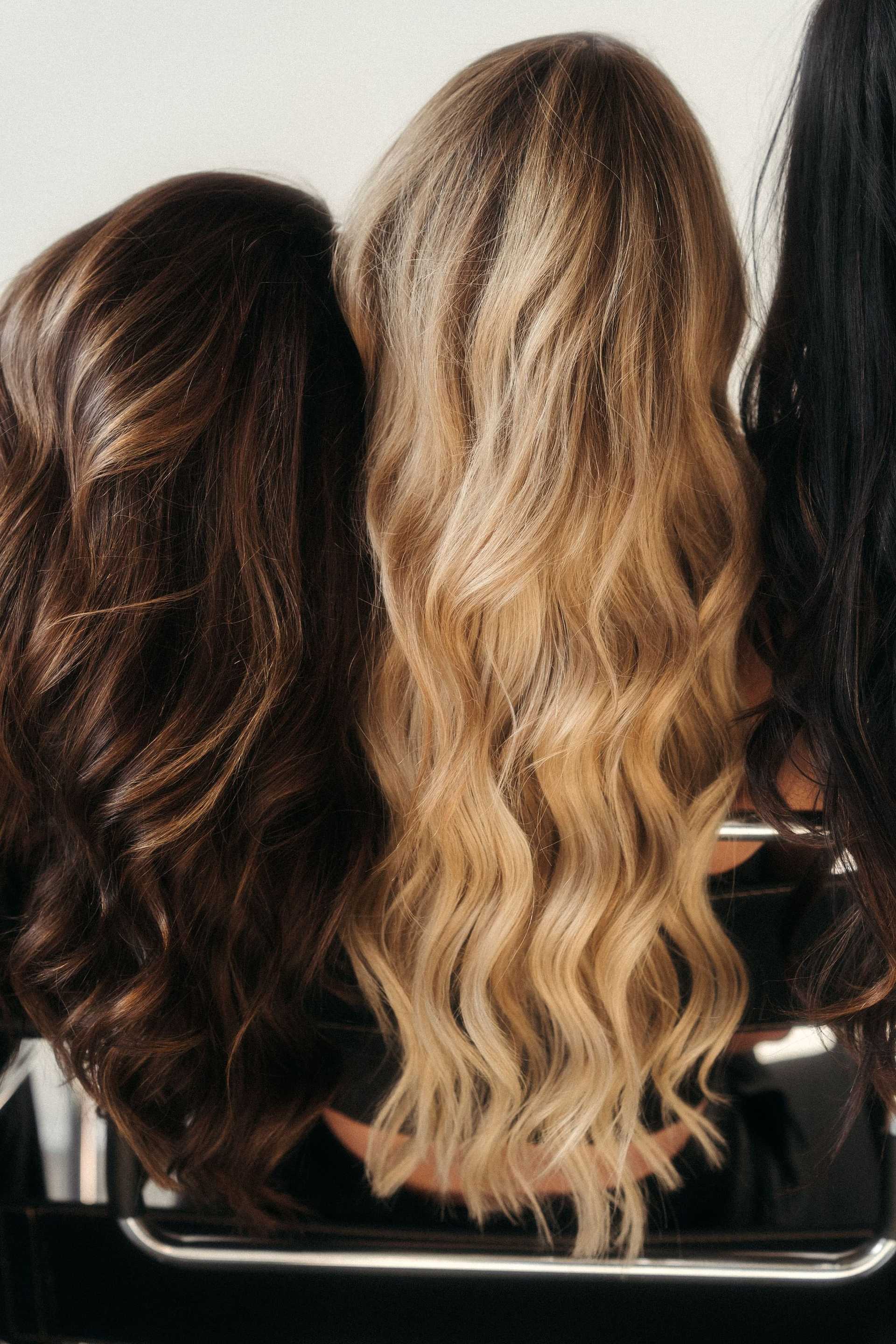 Three women with different shades of wavy hair sit in a row, showing variety in hair color.